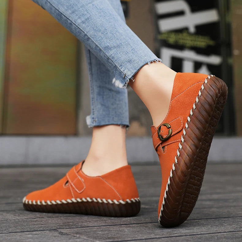 Orange loafers worn with blue jeans on a wooden floor.